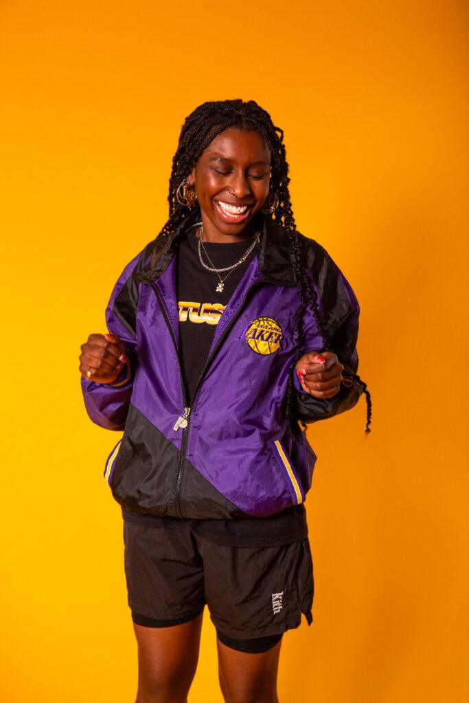 Smiling model in a purple jacket against a yellow backdrop