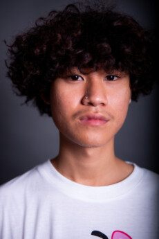 Model Danai looking to camera in a press shot with a big curly hair on a dark grey background in a close up shot